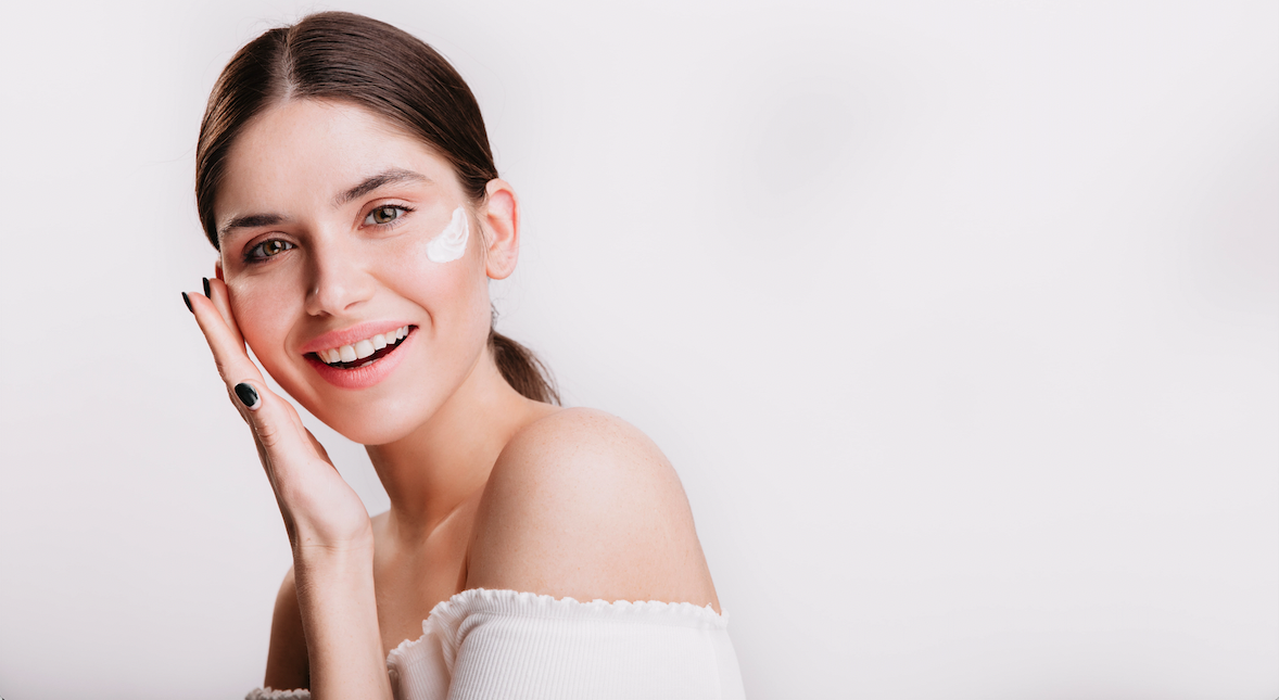 smiling woman puts cream on her face