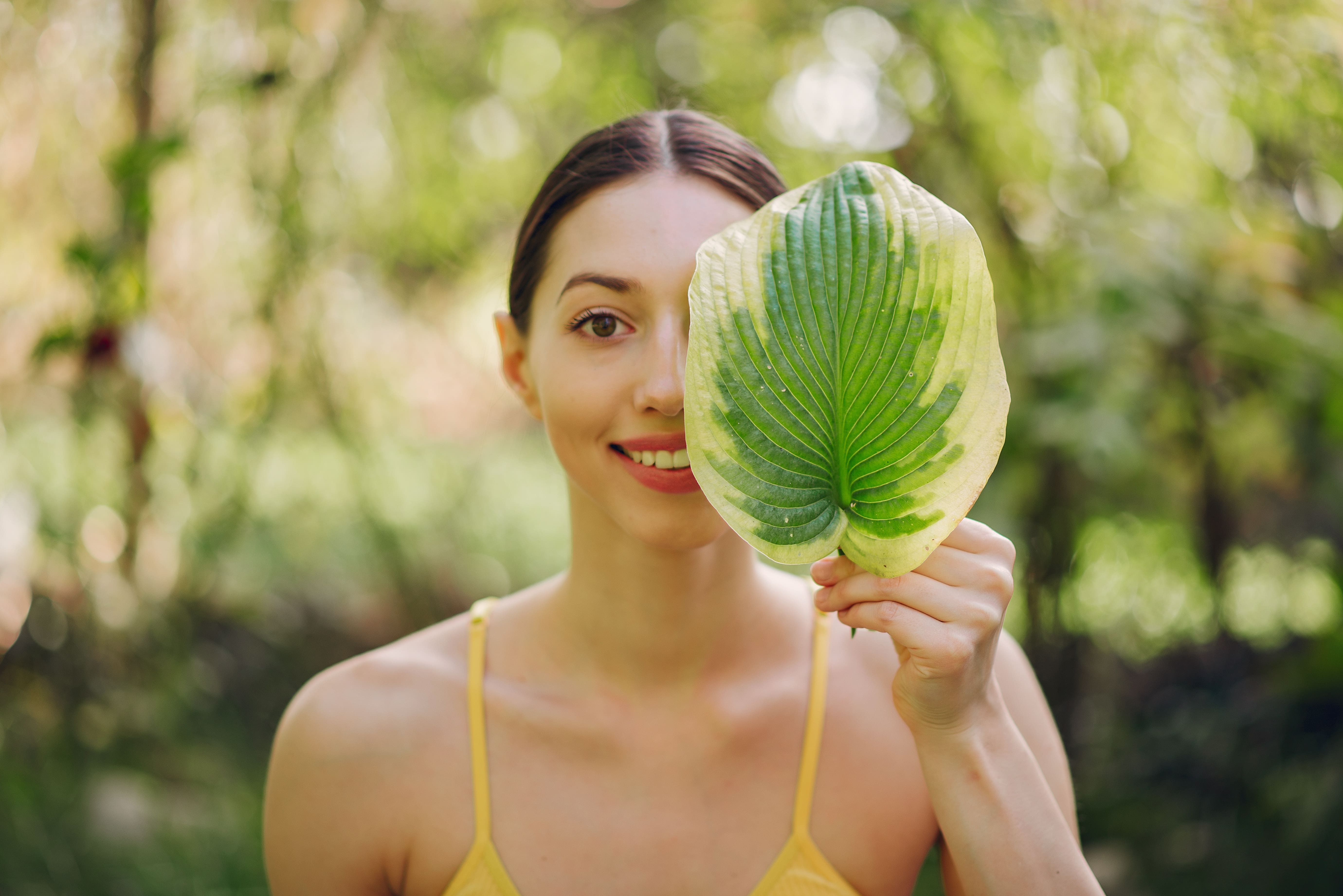 Girl holding green leaf near her face