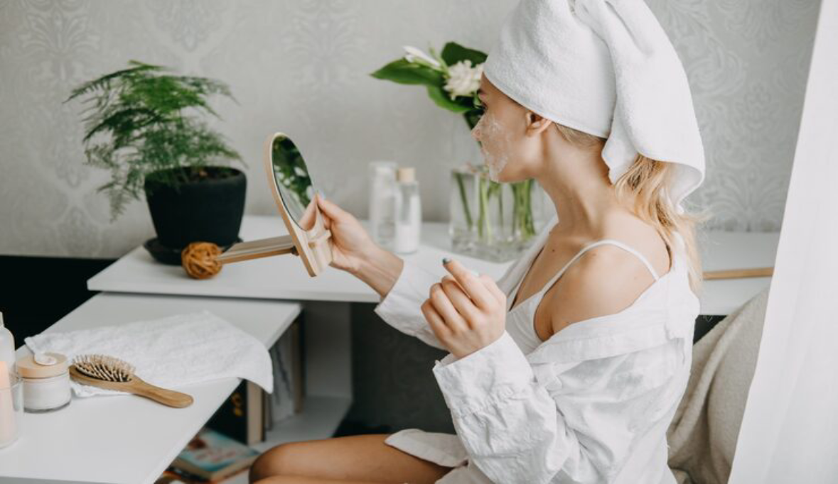 Young woman white towel chilling bedroom making clay facial mask near mirror