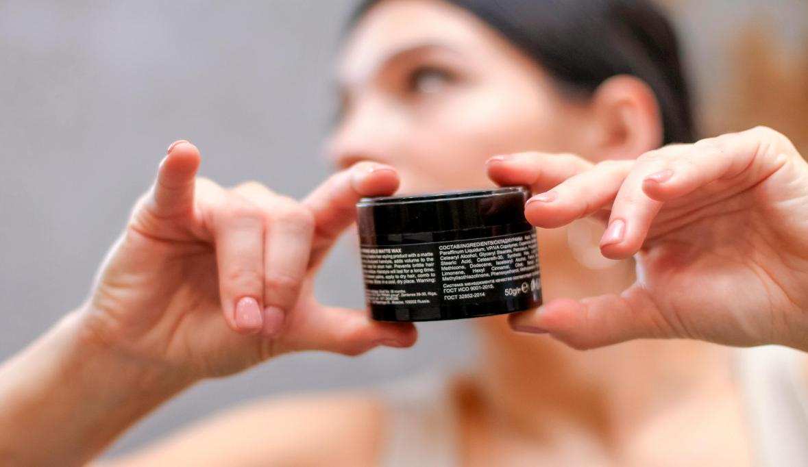 A person with blurred face holds a small skincare or cosmetic product