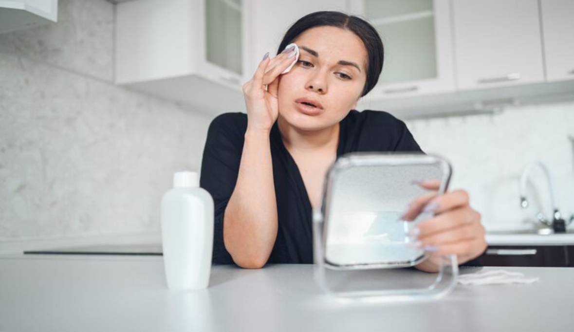 Woman removing makeup from her face with mirror