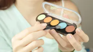 A woman holds a colorful makeup palette and brush