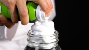 Hands squeezing white shaving cream foam into glass